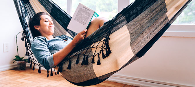 mulher deitada em uma rede e lendo um livro