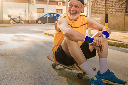 Imagem de um homem idoso sentado encima de um skate sorrindo