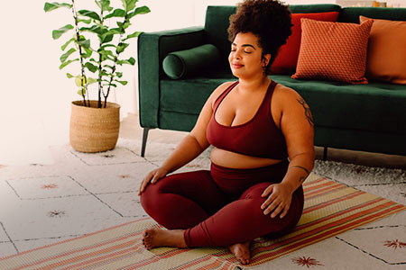 Imagem de uma mulher sentada sobre um tapete, em posição de meditação