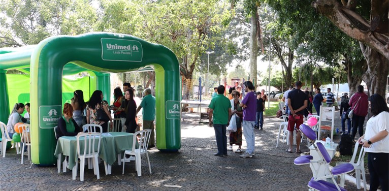 Na imagem, há uma tenda verde inflável, com o logo da Unimed, em um parque, que está repleto de pessoas.