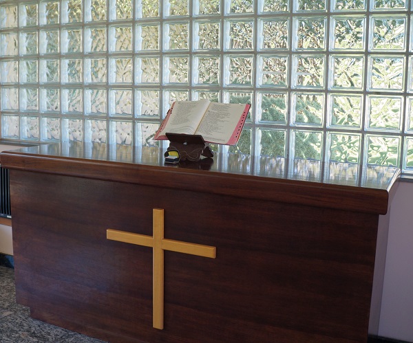 Imagem de um balcão da Capela. Em cima deste balcão, tem uma bíblia aberta em cima de um suporte.