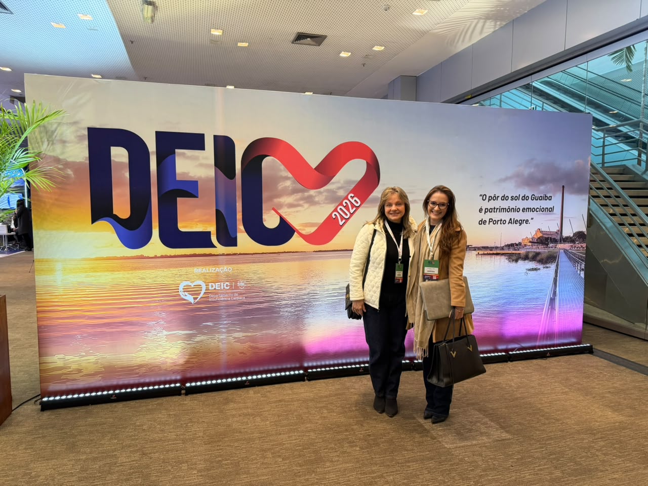 As médicas cardiologistas posam para registro fotográfico diante do painel institucional do congresso DEIC.