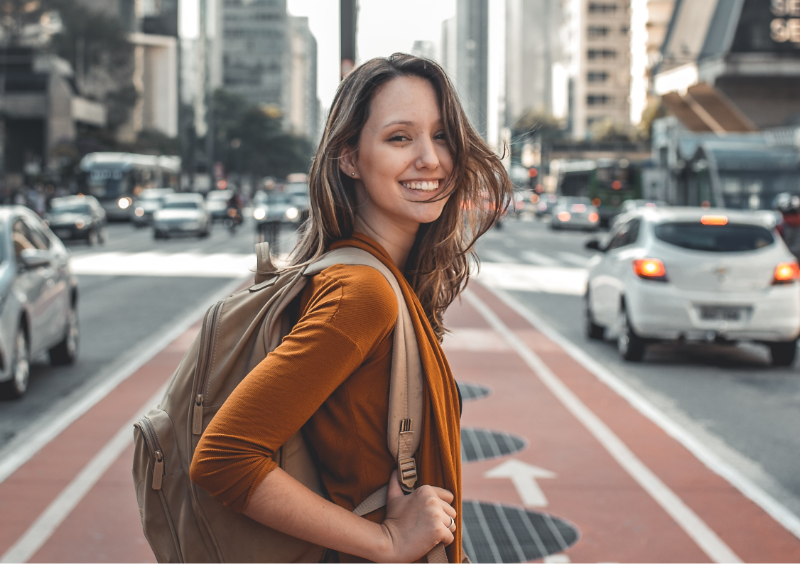 Mulher sorrindo para foto em rua com carros passando.